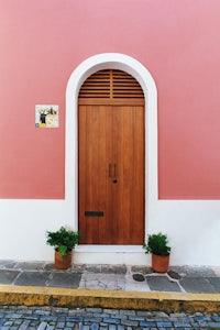 a pink building with a wooden door and potted plants